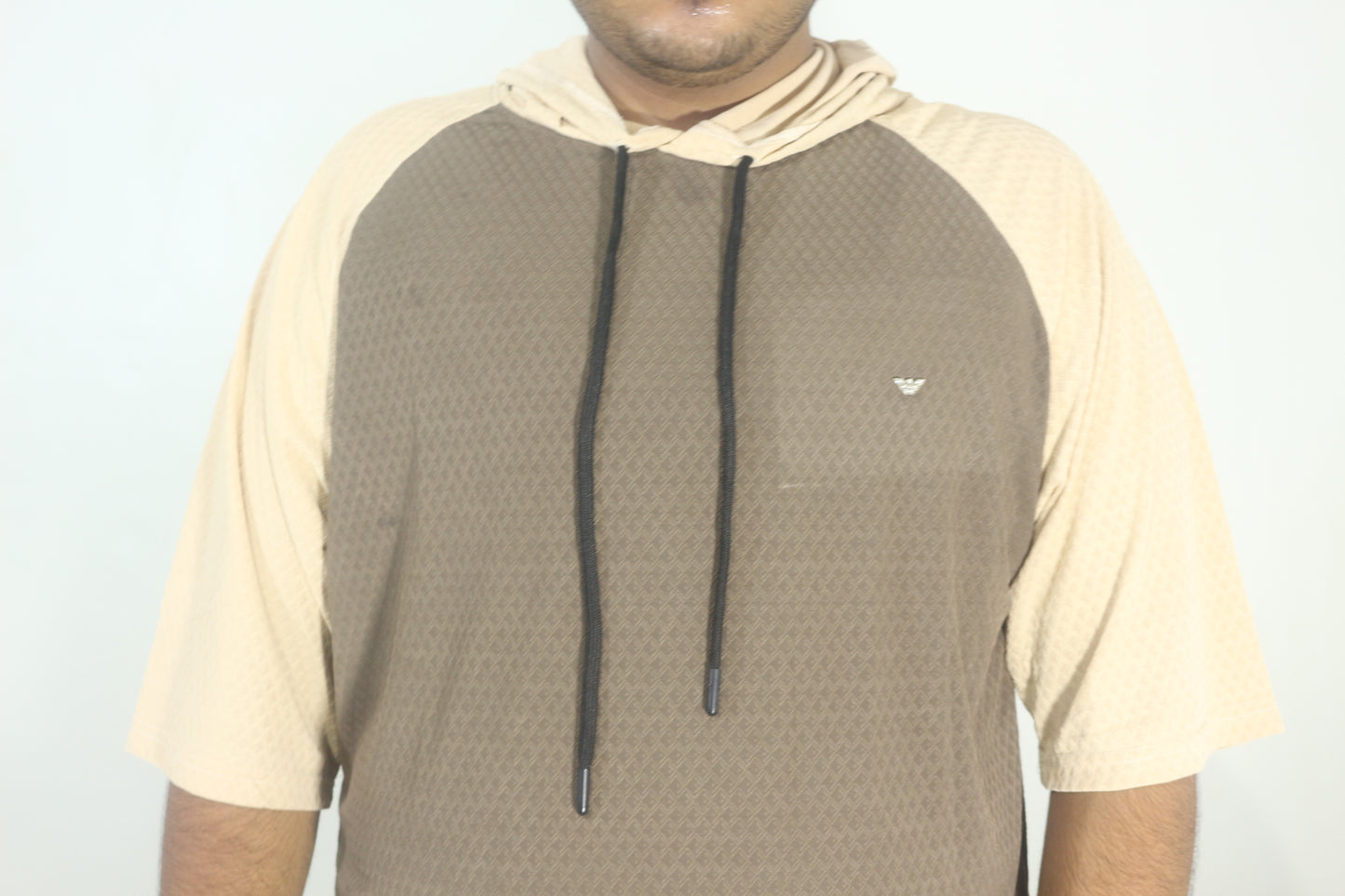 Person wearing a brown and beige hoodie with a brand logo on a light gray background